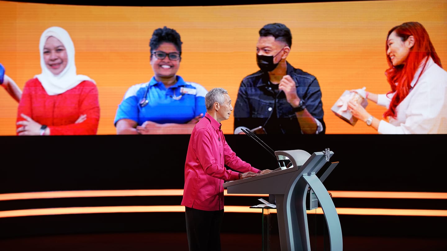 Lee Hsien Loong at podium with people on screen behind.